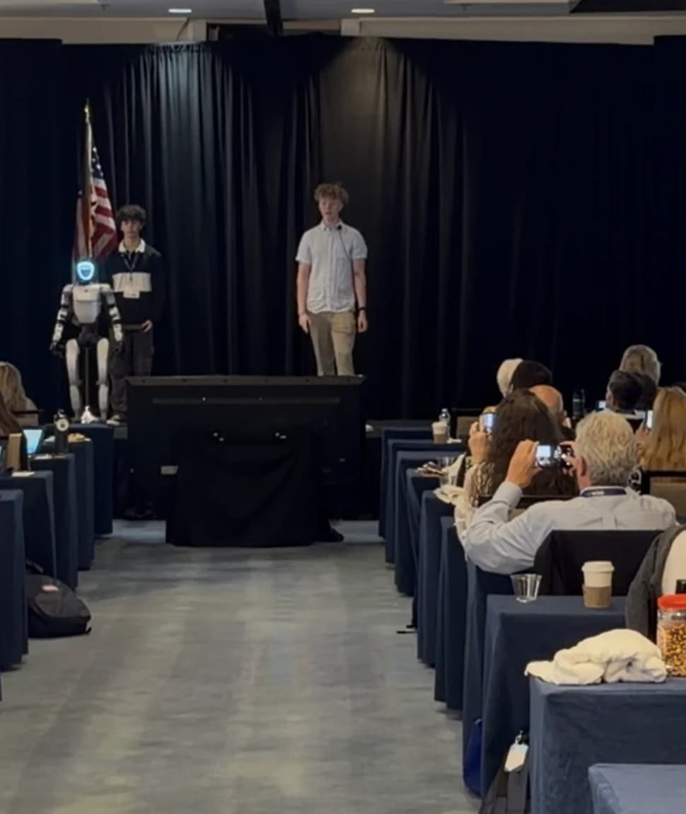 Project Meeseeks on stage beside two presenters during a public demonstration.